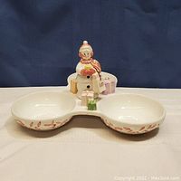 Full view of the white ceramic sectional dish with three compartments and leaf trim, featuring the snowlady centerpiece with gifts.