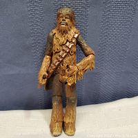 Full frontal view of the Chewbacca action figure standing upright on a white surface with a blue textured backdrop.