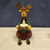 Front view of the Christmas moose tealight holder figurine seated and holding an LED tealight candle.