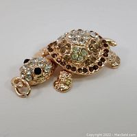 Crystal turtle pendant with clear, green, brown, and black crystals on a gold-tone base. The pendant features a moving head and attachment loop.