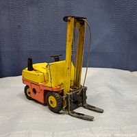 Yellow and orange Dinky Toys Conveyancer forklift toy upright on fabric background
