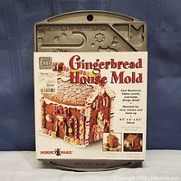 Front view of the gingerbread house mold with attached product label showing gingerbread house image and details