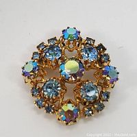 Top view clear photo of the circular mid century brooch showing multicolored crystals and gold setting.