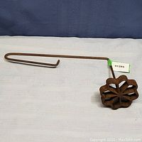 Side view of the old pastry iron showing the long handle and floral mold end.