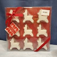 Front view of the unopened soap box containing nine white reindeer-shaped soaps arranged in three rows of three on red background with a red ribbon tied around the packaging.