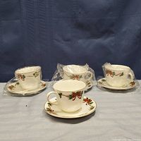 Four Doulton tea cups and saucers arranged on a table, three cups wrapped in plastic, one unwrapped and visible.