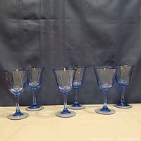 Front view of six blue stemmed glasses arranged in a row, showing their clear bowls and slender blue stems and bases.