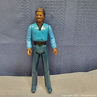 Front view of the Lando Calrissian action figure showing full body from head to feet against a textured fabric background.