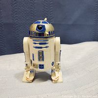 Front view of R2-D2 figure on a light-colored fabric surface, showing detailing and condition