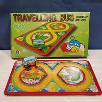 Photo showing the tin wind-up bus toy on the colorful race track board with the original box behind it, highlighting the product name and artwork.