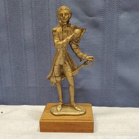 Full view of vintage metal figurine showing gentleman in 18th-century dress holding a hat, standing on wooden base.