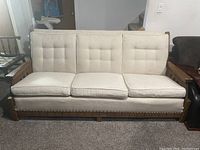 Front-facing view of mid-century rustic style sofa with cream/light beige cushions and wooden frame with armrests.