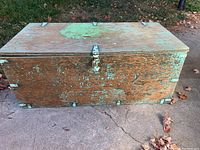 Closed weathered wooden trunk with chipped and faded paint and metal hardware.