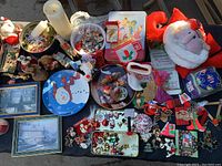 Overview of assorted Christmas plates, tins, ornaments, Christmas decor, and knickknacks arranged on a black cloth base.