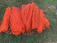 Photo showing rolled and loosely coiled bright orange plastic fencing mesh with diamond-shaped openings on grass.