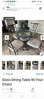 Glass dining table with metal base and four matching metal chairs with beige cushions. Shows spots on cushions and requires cleaning.