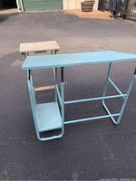 Light blue metal drafting table showing side shelf and lower shelf on pavement