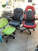 Photo showing three chairs: lime green mesh office chair, black worn leather office chair, black and red gaming chair