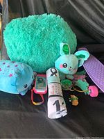 Photo showing the large green fluffy pillow, white bunny plush, small purple skateboard, pink toy phone, rolled fabric, green wristwatch, and small toy figurines.