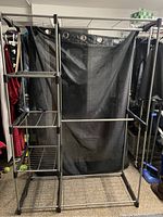 Front view of the full laundry drying rack showing the black metal frame, corner wire shelves and fabric black curtain behind it.