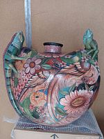 Front view of the large pottery vase with colorful hand-painted floral and bird motifs and an iguana figure on the left side.