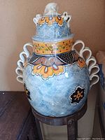 Front view of large hand-painted Mexican pottery vase with lid on metal stand