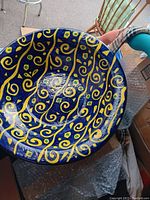 Top view of large pottery bowl showing vibrant blue, yellow, and green swirl pattern with glossy finish. Shows marks and dirt spots needing cleaning.