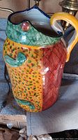 Photo of brightly colored ceramic pottery pitcher with frog design and multicolored patterned glaze including green, yellow, and red sections