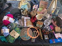 Full view of lot showing various yarn skeins, wolf statue, cup holder, jewelry boxes, glassware, beads, frying pan, vintage tins, and books.