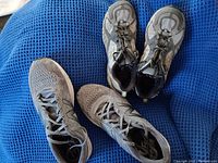 Top view of two pairs of New Balance running shoes with visible signs of wear and dirt, placed on a blue textured fabric.