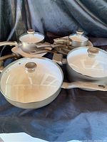 Full set of pots with five lids on a dark backdrop, showing various sizes and beige handles