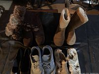 Photo showing various shoes and boots arranged on a floor including furry brown boots, Bearpaw boots, black dress shoes, and white shoes.