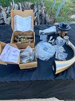 Wide view of assorted new Price Pfister tub and shower parts laid out on black cloth. Includes valves, handles, spout, and mounting parts with packaging and paper instructions.