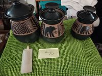 Set of three stoneware canisters (small, medium, large) with lids. Black and natural clay sculpted geometric and bear designs. Large lid has a repair.