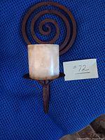 Metal wall sconce with light-colored candle holder cover and spiral metal backplate on blue fabric background with lot number card.