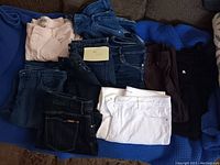 Nine pairs of women's pants and shorts in various colors laid out on a blue fabric surface.