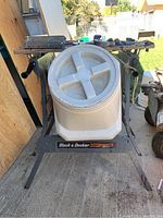 Black & Decker Workmate portable work center with the storage bin on top; workmate made of metal with foldable legs, storage bin is large gray plastic with circular molded lid, showing chew damage and dirt.
