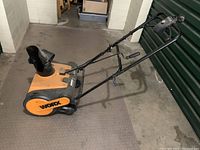 Side angle view of the orange and black Worx electric snowblower showing overall condition and handle design.