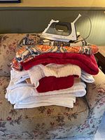 Lot consisting of multiple smaller blankets stacked on a floral patterned couch with a Rowenta iron placed on top.
