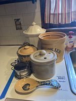 Canisters grouped together on kitchen counter showing assortment including 'Cookies' canister, large faceted white canister, spoon rest, small metal canister, and other ceramic canisters