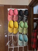 Five pairs of Crocs in pink, black, yellow, green, and blue hanging on a door organizer.