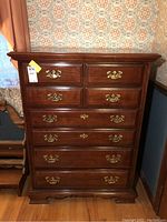 Front view of the dark wooden dresser showing six drawers with brass handles and the overall shape and finish.