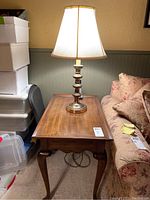 Full view of rectangular wood end table with cabriole legs and gold plated lamp on top next to sofa.