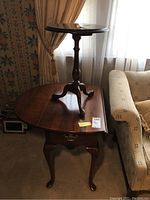 Drop leaf wooden end table with one drawer and cabriole legs under the round pedestal table