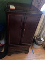 Front view of a tall wooden jewelry chest with two closed doors and a single drawer at the bottom