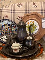Photo showing four platters, including wooden framed ceramic with floral design, a blue and white platter, and a large silver-tone platter with Sheridan silver-plated tea set placed on top.