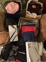 Boxes and piles of various pocketbooks including fabric, wooden handled and leather handbags arranged on a couch.