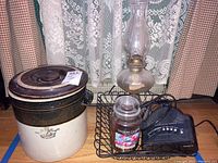 View of entire lot showing ceramic pot, Yankee Candle, Sony radio, metal basket, and glass hurricane lamp in front of lace curtain.