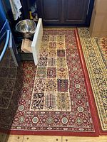 Full view of the red wool area rug on a floor showing the patchwork design and the floral border.
