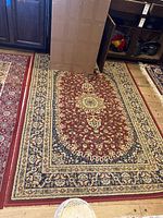Full view of red wool area rug showing overall pattern and colors on wooden floor.